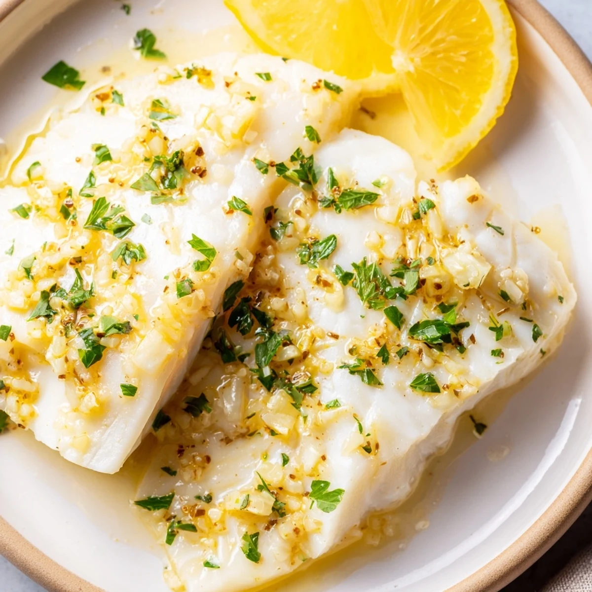 Flaky baked halibut with lemon butter, served with fresh parsley and a lemon wedge, looks delicious.