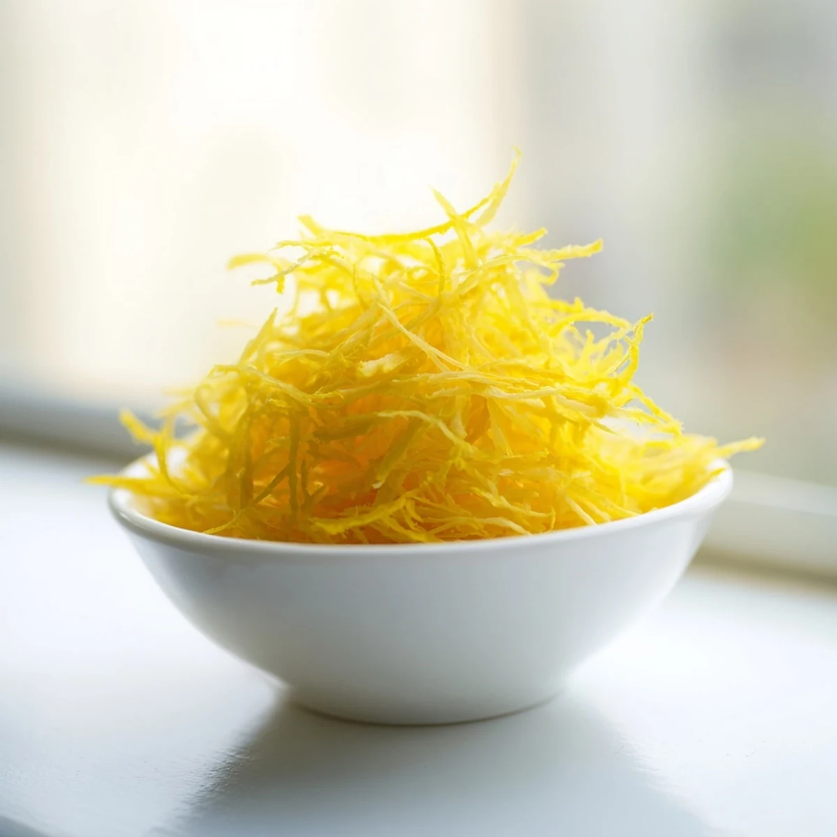 Bright yellow lemon zest, finely grated in a small bowl, ready to add fresh citrus flavor.
