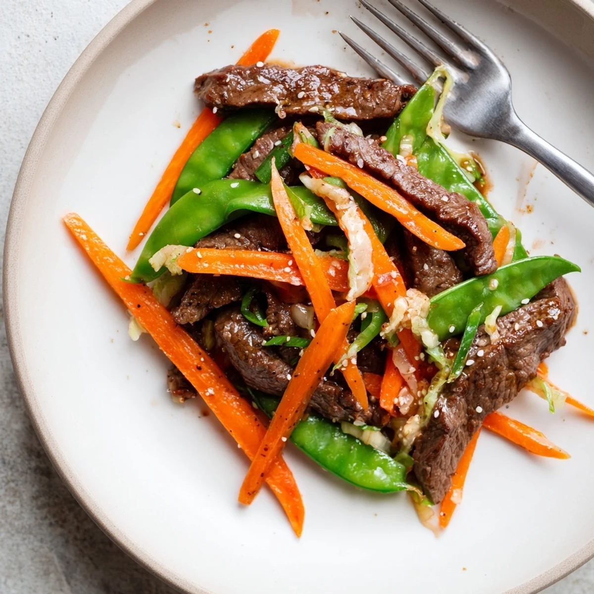 Tender beef stir fry with snow peas and carrots in a rich, glossy sauce, ready to serve.