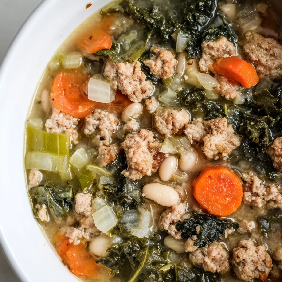 Hearty Turkey Sausage and Kale Soup steaming in a rustic bowl, showcasing browned sausage crumbles and vibrant green kale leaves in a rich tomato broth.