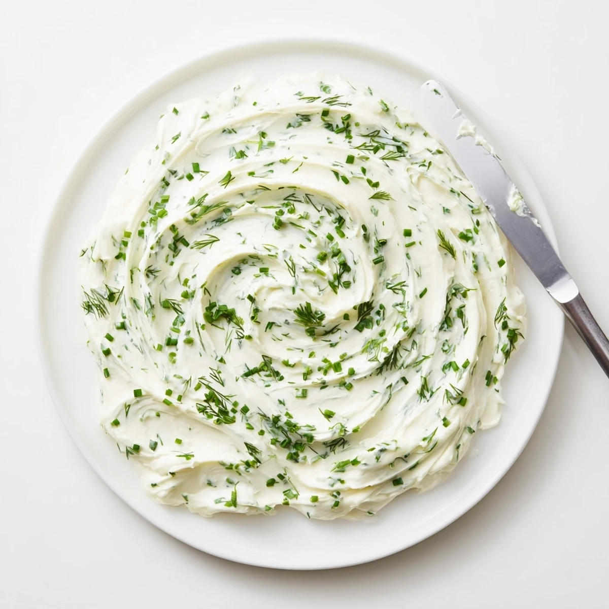 Ein cremiger Creamy Appetizer Spread Dip mit Kräutern und Knoblauch, serviert auf goldenen Baguettestücken neben einer kleinen Gabel für den perfekten Partysnack.