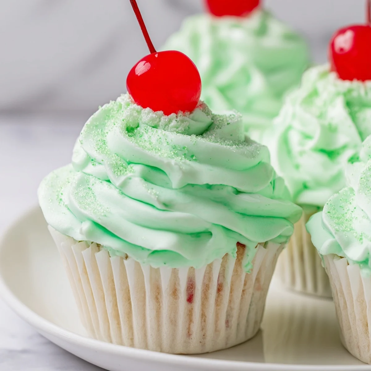 Fluffy Shamrock Shake Cupcakes topped with green mint frosting and a maraschino cherry.