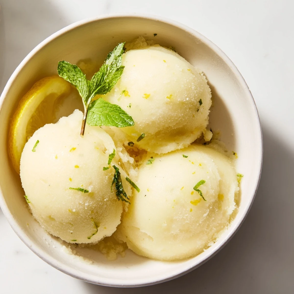 Frisch zubereitetes Lemonade Sorbet mit Minze zeigt eine cremige, hellgelbe Kugel in einer Schale.