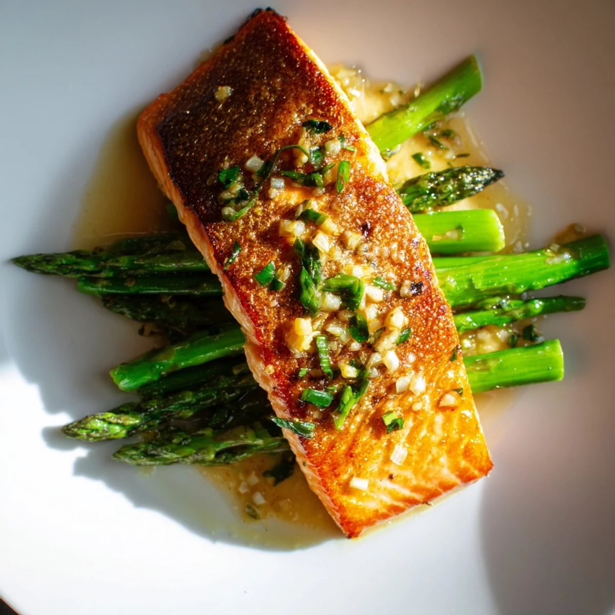 Gesalzene, goldbraun gebratene Lachsfilets liegen auf knackigem Spargel, übergossen mit einer glänzenden Zitronen-Butter-Sauce.