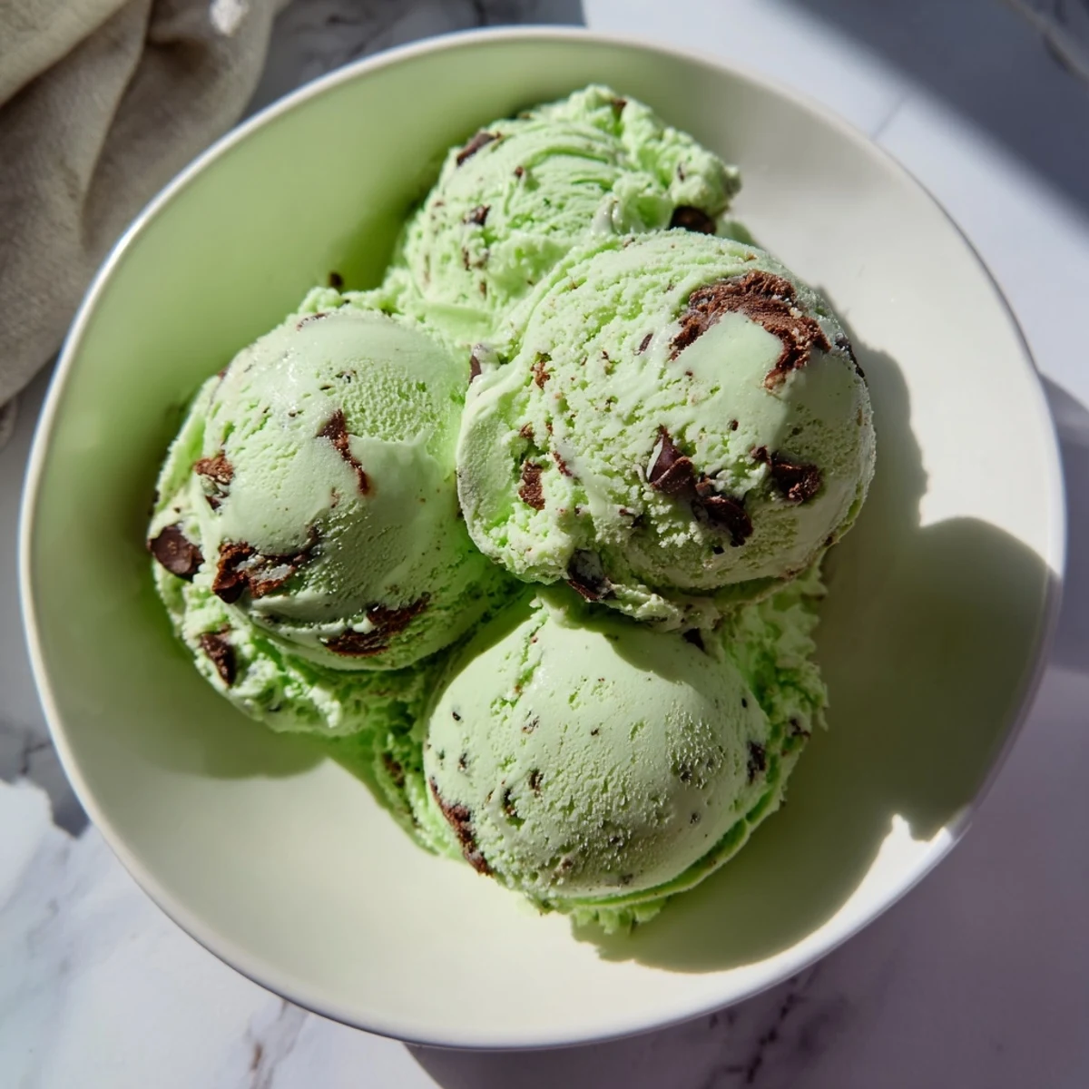 Serving a scoop of Green Mint Chocolate Chip Ice Cream in a chilled glass dish, garnished with mint sprigs.