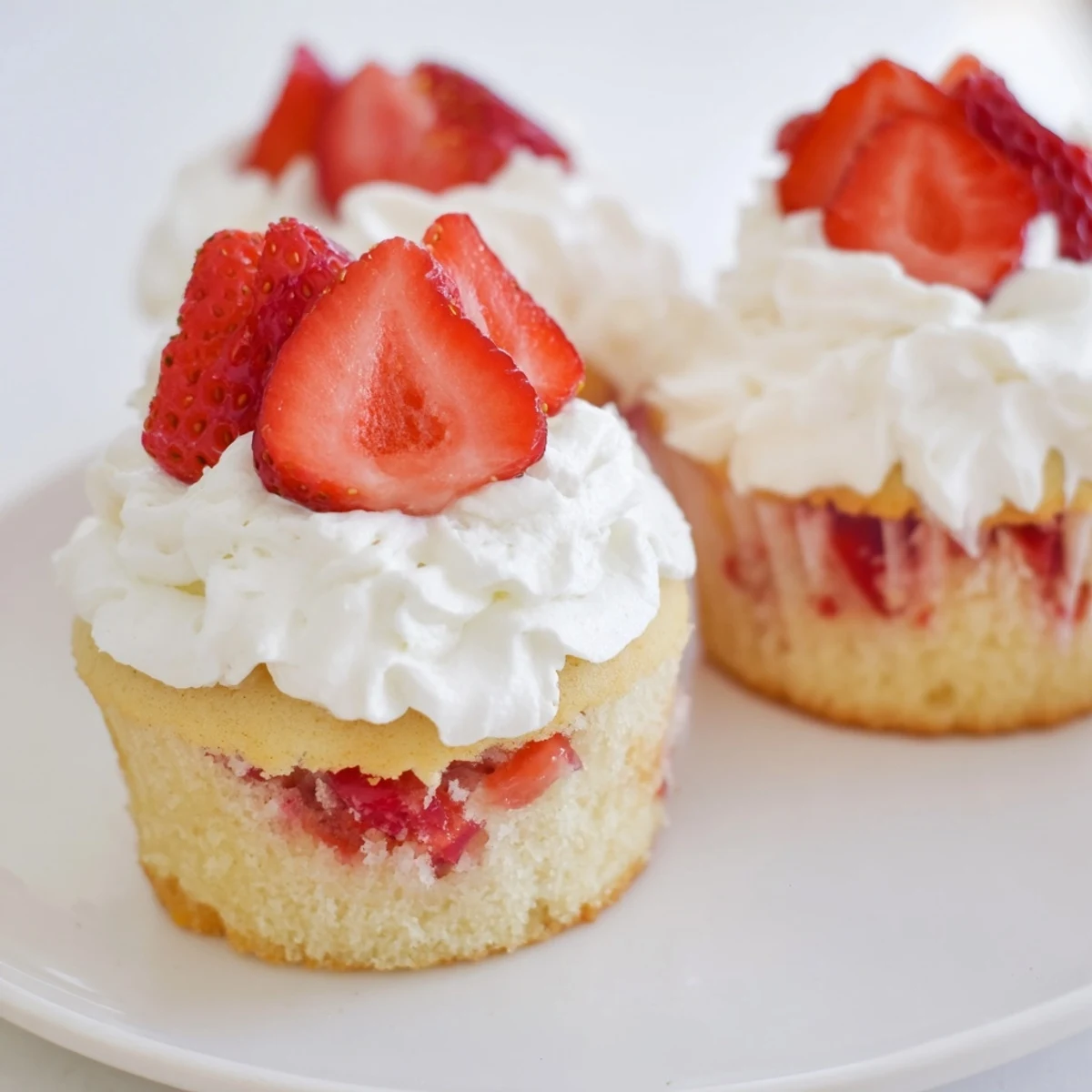 Feuchte Vanille-Muffins der Strawberry Shortcake Cupcakes with Frosting zeigen rote Fruchtfüllung und gazeniger Sahneglasur, perfekt für Sommerfeiern.