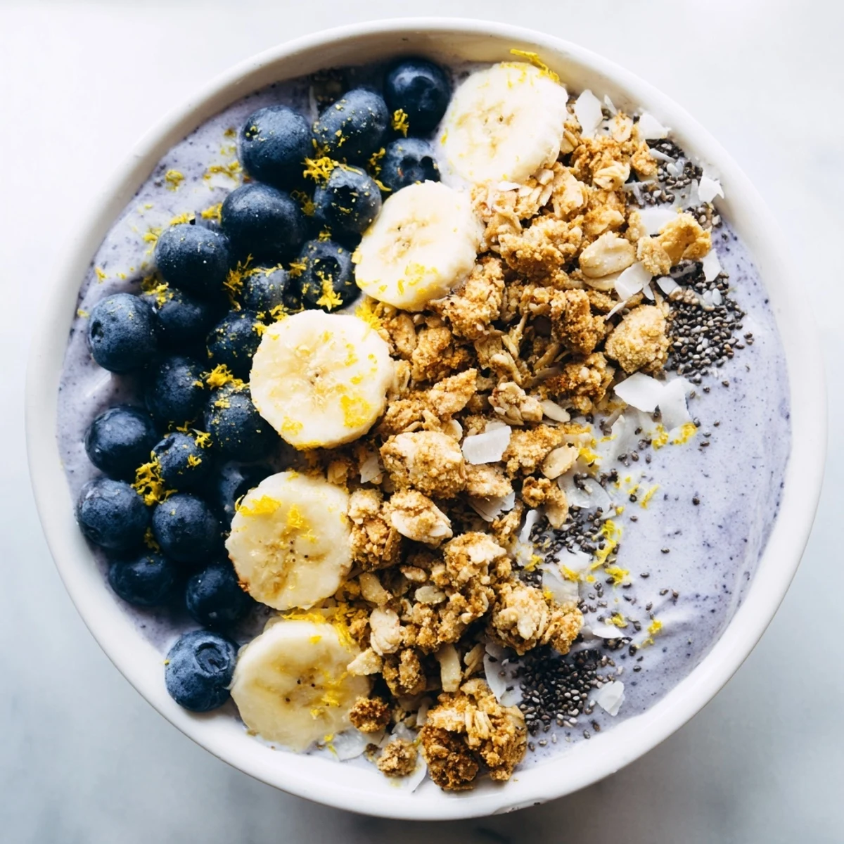 Lemon Blueberry Smoothie Bowl with Granola topped with sliced banana, coconut flakes, and chia seeds for extra crunch.
