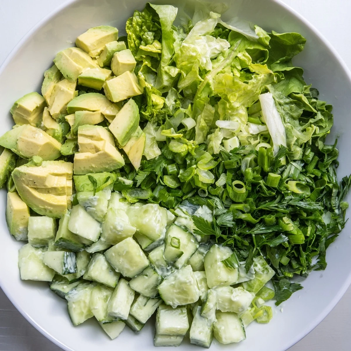 Grüner Goddess Salat mit Avocado und Gurke, garniert mit Petersilie und grünem Zwiebelkranz auf weißem Teller.