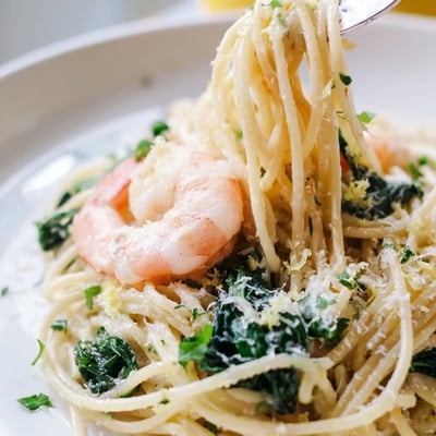 Goldene Shrimp und Spinat in zitroniger Nudelsauce; serviert mit einer Scheibe knusprigem Baguette.