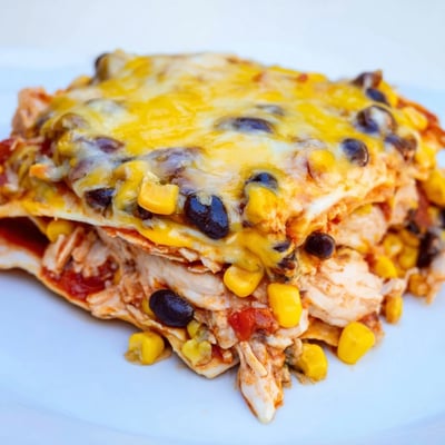 Hearty Chicken Enchilada Casserole with Cheese ready to slice, served with sour cream and lime wedges on the table.