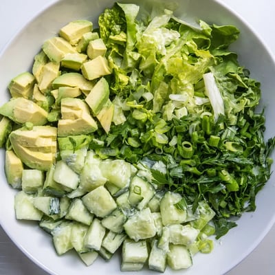 Grüner Goddess Salat mit Avocado und Gurke, garniert mit Petersilie und grünem Zwiebelkranz auf weißem Teller.