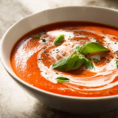 Die heiße Cremige Tomatensuppe mit frischem Basilikum dampft in einem Topf, begleitet von Brot und Olivenöl.